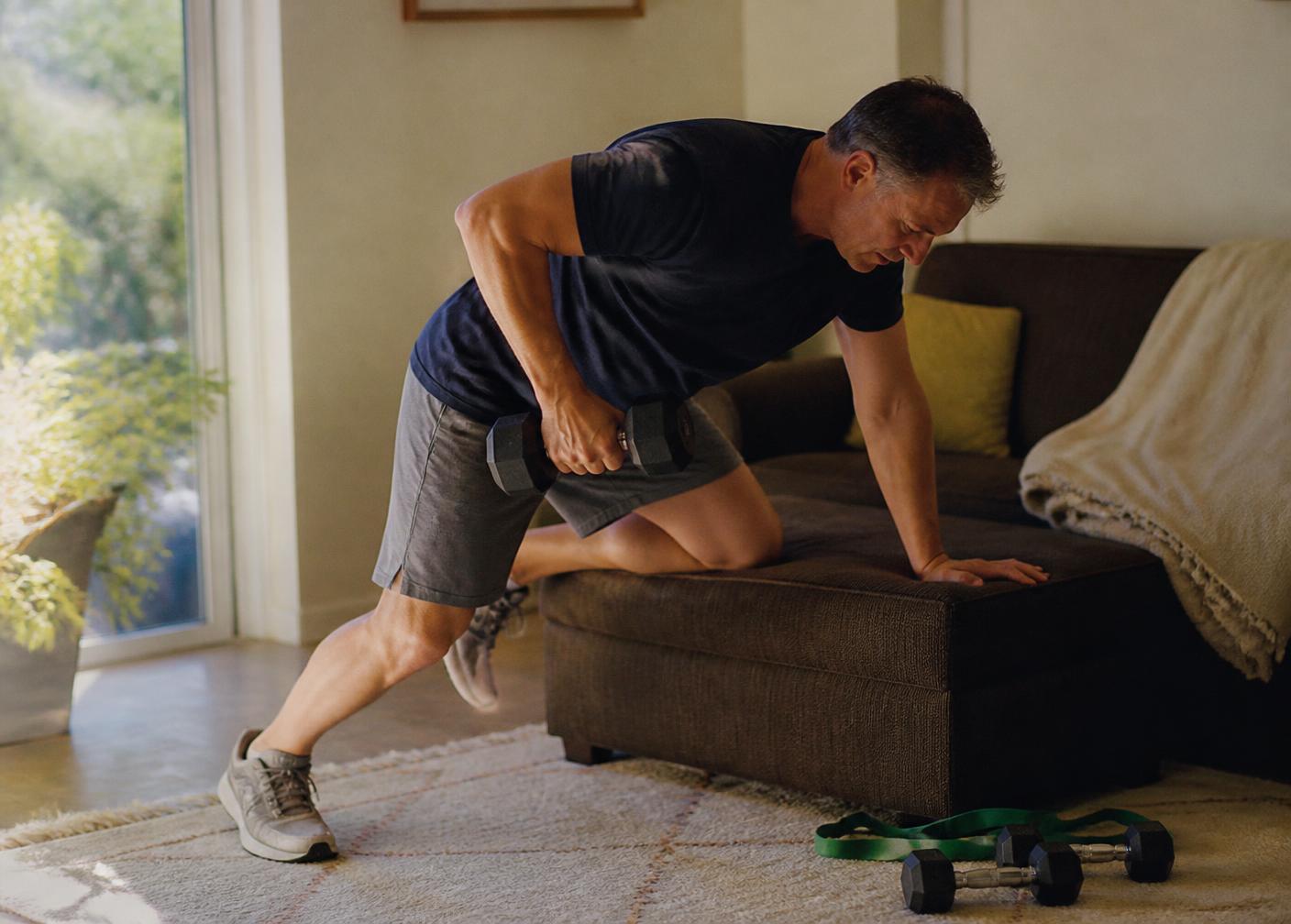 A man in his fifties doing a single-arm dumbbell row in his living room